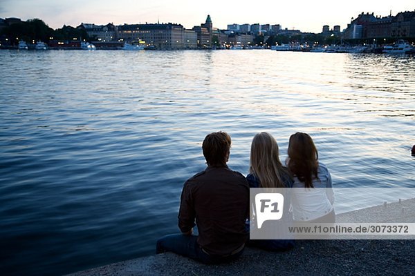 Three friends sitting on a quay-edge Stockholm Sweden.