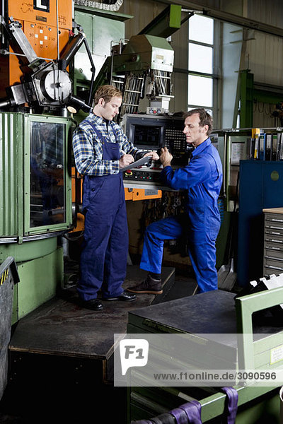 Two men in a metal parts factory reviewing a clipboard