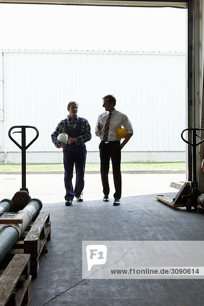 A manager talking to a manual worker in a warehouse doorway  back lit