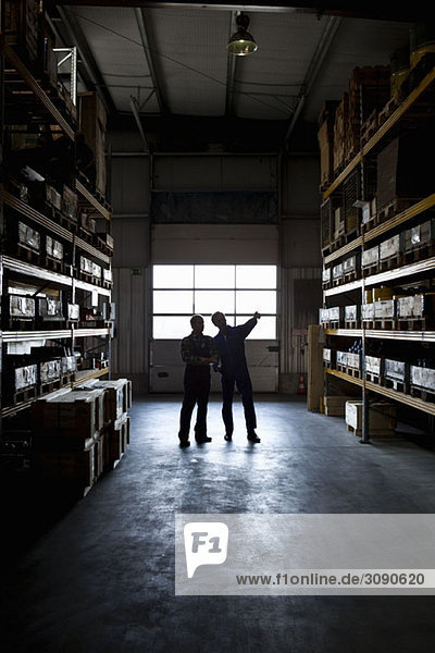 Two manual workers in a metal parts warehouse