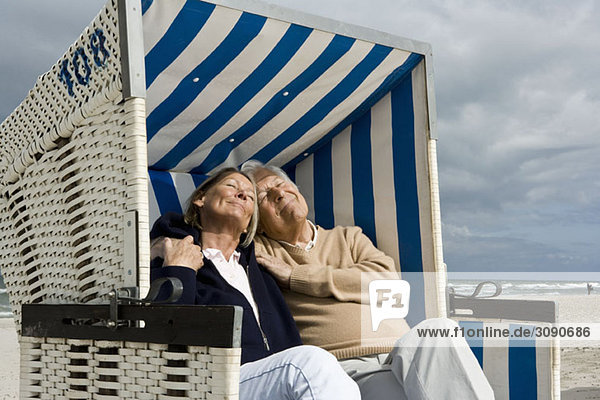Ein älteres Paar sitzt zusammen in einem Strandkorb mit Kapuze.