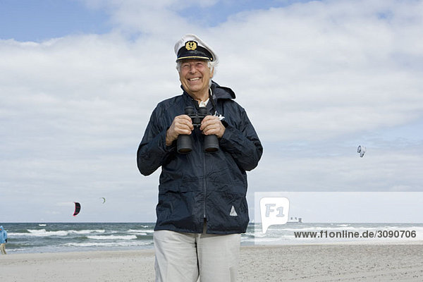A senior man on a beach holding binoculars