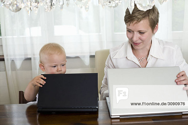 Eine Mutter und ein Kleinkind öffnen ihre Laptops  Seite an Seite.