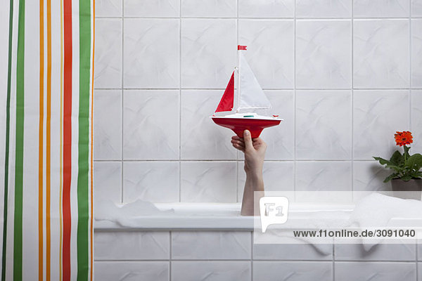 A human hand sticking out of a bathtub holding a toy boat