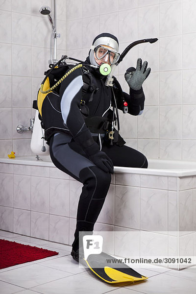 A scuba diver making the OK sign while sitting on the edge of a bathtub