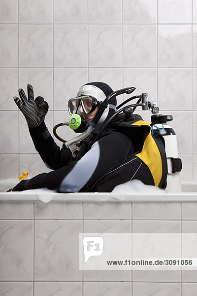 A scuba diver sitting in a bubble bath giving the OK sign