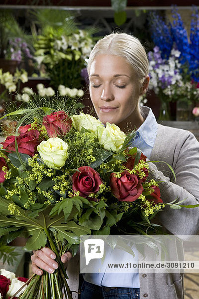Eine Frau  die einen Blumenstrauß in einem Blumenladen riecht.