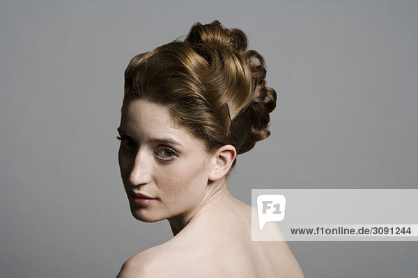 Porträt einer jungen Frau mit eleganter Frisur  die über die Schulter schaut.