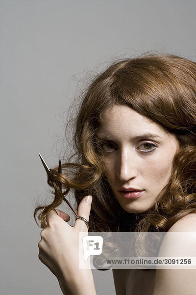 Eine junge Frau hält eine Schere und schneidet sich die Haare.