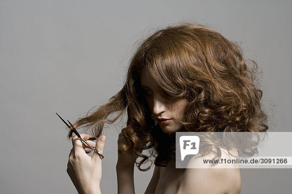 A young woman holding scissors and cutting her hair