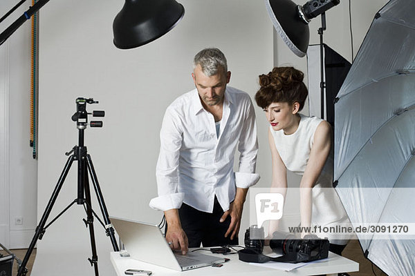 A model and a photographer looking at a laptop computer on the set of a fashion shoot