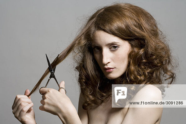 Porträt einer jungen Frau  die eine Schere an den Haaren hält.