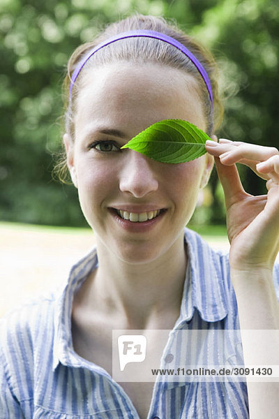 A young woman covering her eye with a leaf