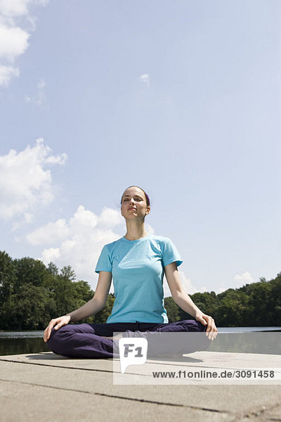 Eine junge Frau  die Yoga auf einem Steg praktiziert.
