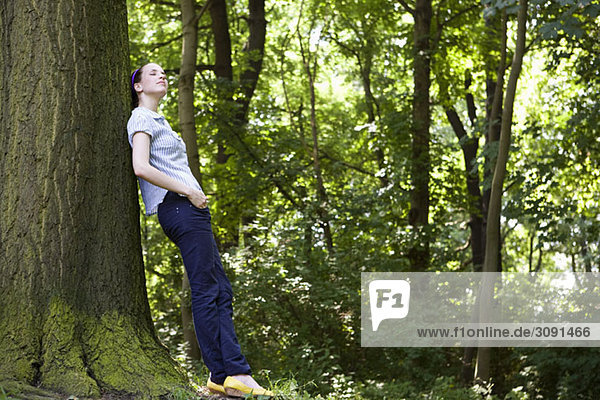 Eine junge Frau  die sich an einen Baum lehnt.