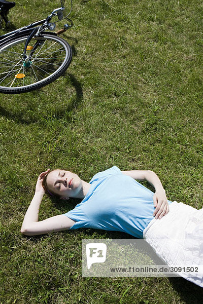 Eine junge Frau  die im Gras in der Nähe eines Fahrrads liegt.