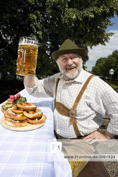 Ein traditionell gekleideter deutscher Mann in einem Biergarten  der sein Bierglas in Toast hebt.