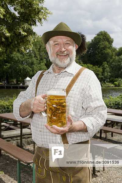 Ein traditionell gekleideter deutscher Mann in einem Biergarten mit einem Bierglas