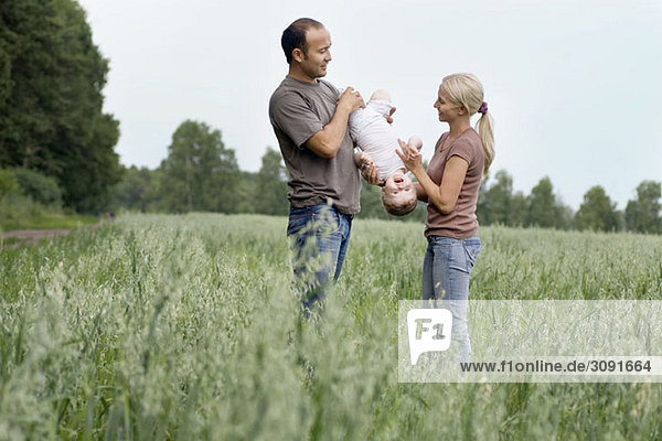 Zwei Eltern  die mit ihrer Tochter auf einem Feld spielen.