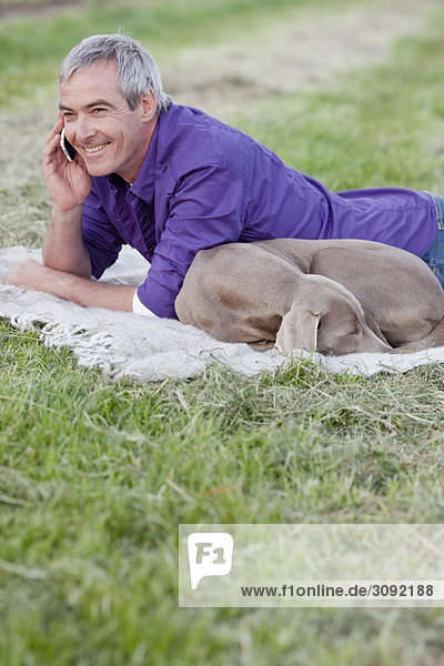 Mann mit Hund am Telefon im Gras