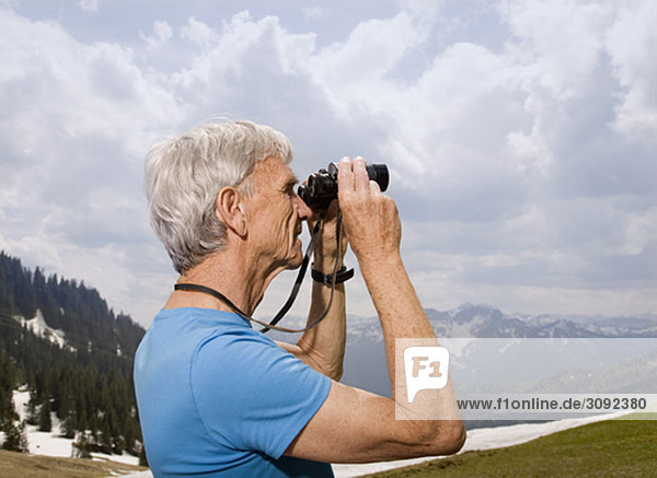 senior man with binoculars in mountains