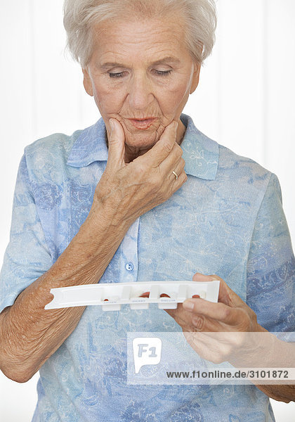 Seniorin schaut ratlos auf ihren Tablettenplaner