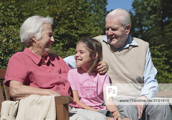 Großeltern sitzen mit Enkelin auf Parkbank  lachen