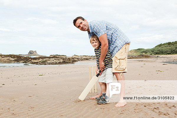 Vater und Sohn spielen Cricket am Strand