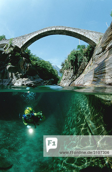 Scuba diver in the Verzasca river with stone bridge in the background  Tessin  Switzerland  underwater shot