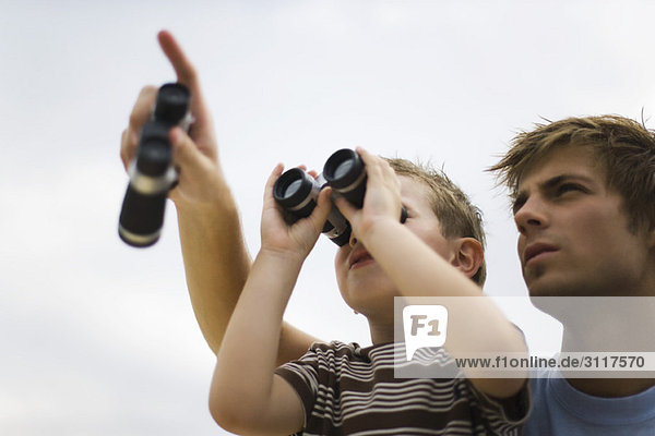 Father and son using binoculars  man pointing skyward