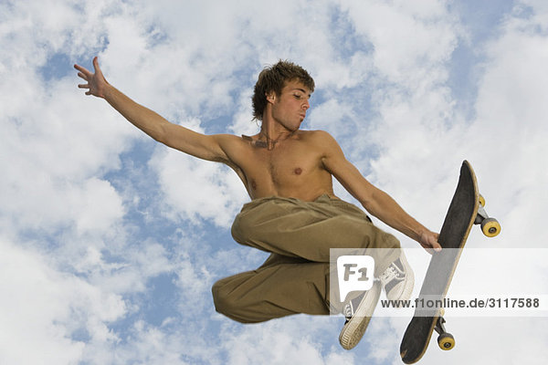 Junger Mann springt in der Luft mit Skateboard