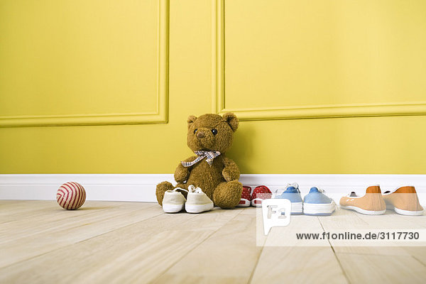 Teddybär auf dem Boden sitzend mit mehreren Paar Schuhen  Ball in der Nähe