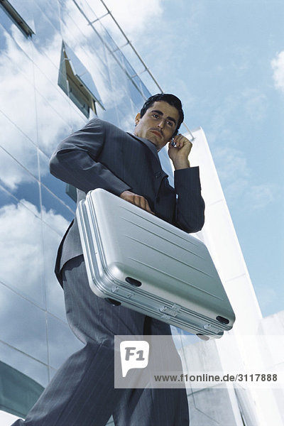 Businessman carrying briefcase using cell phone outside office building