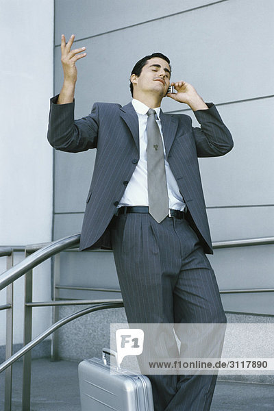 Businessman leaning against railing and using cell phone  making frustrated gesture with hand