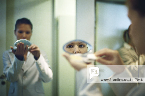 Woman holding powder compact putting on makeup  looking at camera in reflection in mirror