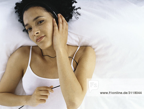 Woman lying on bed listening to headphones