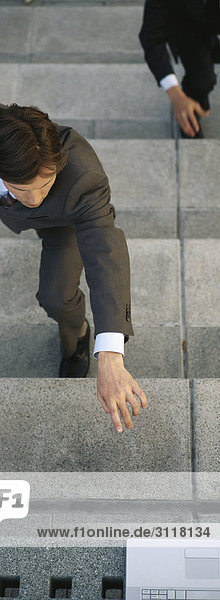 Geschäftsleute hocken auf Stufen  die nach einem Laptop greifen  der oben auf der Treppe steht.