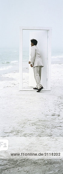 Man opening and entering door placed on beach