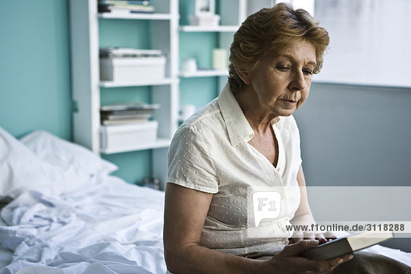 Seniorin sitzend im Schlafzimmer mit Blick auf das Buch