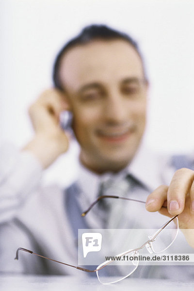 Geschäftsmann am Telefon der eine Brille in der Hand hält.