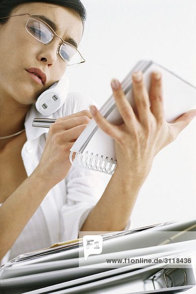 Frau am Telefon beim Schreiben von Notizen im Notizblock