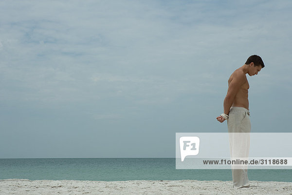 Mann am Strand stehend  Kopf unten  Hände hinter dem Rücken gefesselt  Seitenansicht