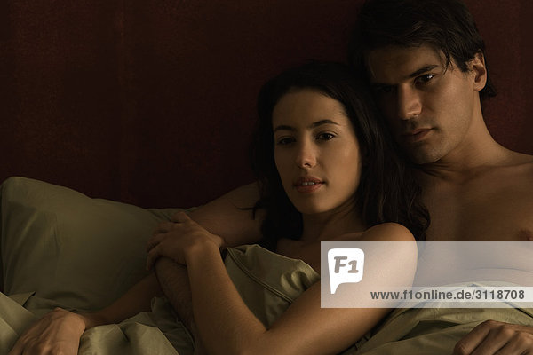Paar liegt zusammen im Bett  der Arm des Mannes um die Schulter der Frau.