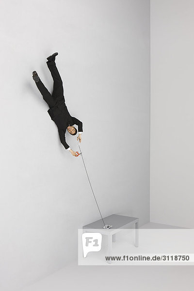 Geschäftsmann schwebend auf dem Kopf stehend mit Festnetztelefon  Schneidekabel mit Schere