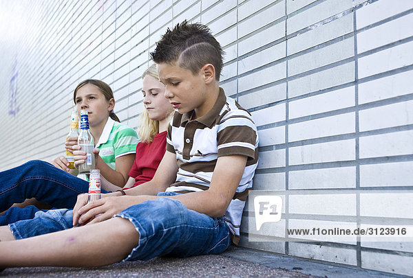 Drei Kinder sitzen auf dem Boden mit Flaschen in der Hand  Flachwinkelansicht