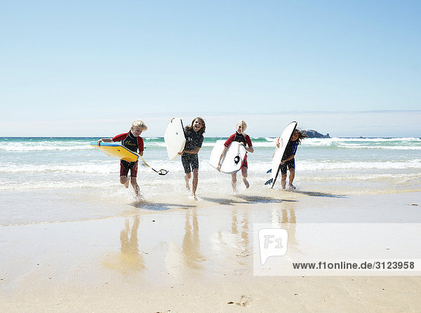 Kinder mit Surfbrettern rennen aus dem Wasser  Frontal
