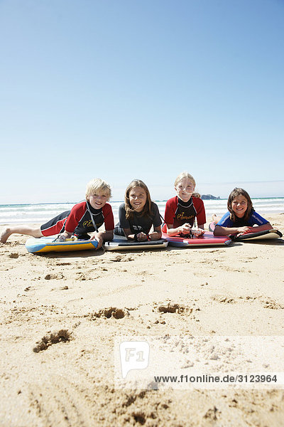 Children lying with surfboards on the beach  front view