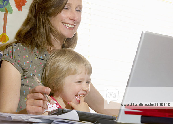 Mädchen auf dem Schoß der Mutter beim Blick auf den Computer