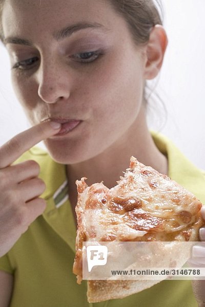 Young woman with partly eaten slice of pizza licking her finger