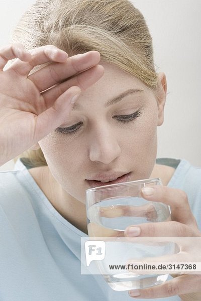 Frau mit Kopfweh trinkt Glas Wasser